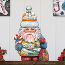 Decorative Christmas gnome Santa claus with colorful hat, scarf and candy cane on a wooden shelf against a white wall.
