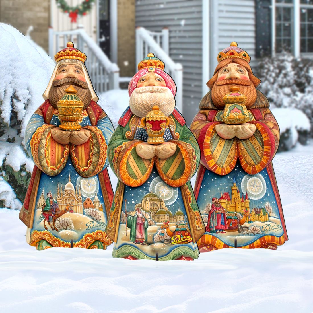 Three hand-painted Christmas Three Kings garden statues standing in a snowy outdoor setting in front of a house.