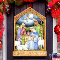 Decorative nativity scene with 'O Come Let Us Adore Him' text on a door with red holiday decorations.