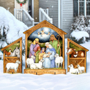 Outdoor Christmas illustrated nativity scene decorative sign displayed in the snow in front of a house. The wooden-framed sign shows Mary, Joseph, baby Jesus, animals, and angels under a glowing star, with the inscription 'O COME LET US ADORE HIM' at the bottom.