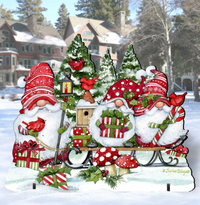 A festive Christmas yard sign featuring gnomes on a sled with wrapped gifts, candy canes, red birds, evergreen trees, and mushrooms, set against a snowy residential background.