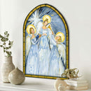 Arched stained-glass-style wall art showing three angel figures in light blue robes with gold halos and rays of light, displayed above a white mantel with decorative vases, books, and ornaments.