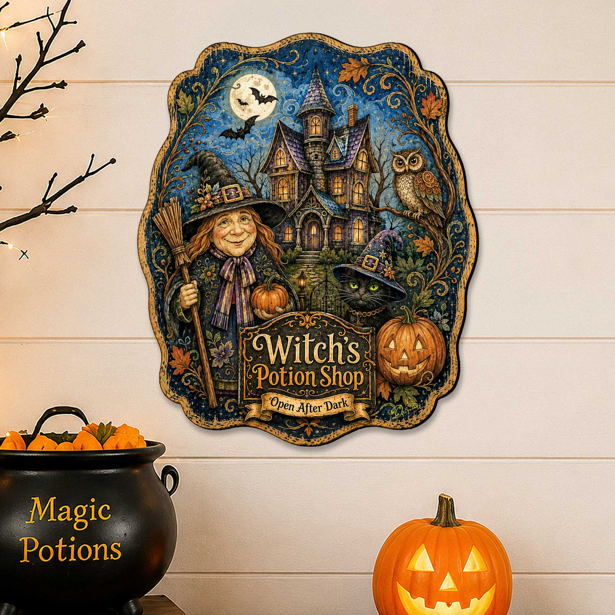 A decorative wall sign featuring an illustrated witch, haunted house, owl, pumpkin, and the text 'Witch's Potion Shop' displayed on a wood surface above a black cauldron and a glowing jack-o'-lantern against a white shiplap wall.