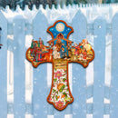 Decorative Christian cross with nativity scene design on a white picket fence in a snowy landscape.