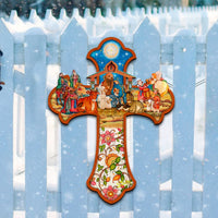 Decorative Christian cross with nativity scene design on a white picket fence in a snowy landscape.