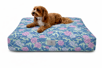 A small brown dog lies on a rectangle Designer Pet Bed with a Pink and Green Large Floral cover with a Country, Cottagecore style on a plain white background.