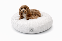 A small brown dog lies on a Designer Round Pet Bed in a Modern design of White & Beige Simple Geometric lines on a white background.