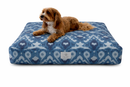 A small brown dog lies on an Ethnic Ikat Maximalist Patterned Designer Pet Bed in navy, medium and Light Blues on a clean white background.