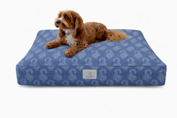 A small brown dog lies on a rectangular Designer Pet Bed with a Denim Blue Floral Paisley design against a clean white background. 