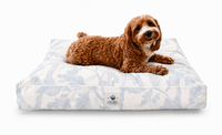 A small brown dog on a Designer Pet Bed in an Organic Modern Botanical Blue/Gray Watercolor style on a plain white background.