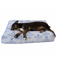 A small black and white dog lies stretched out on a rectangle blue floral dog bed against a plain white background.
