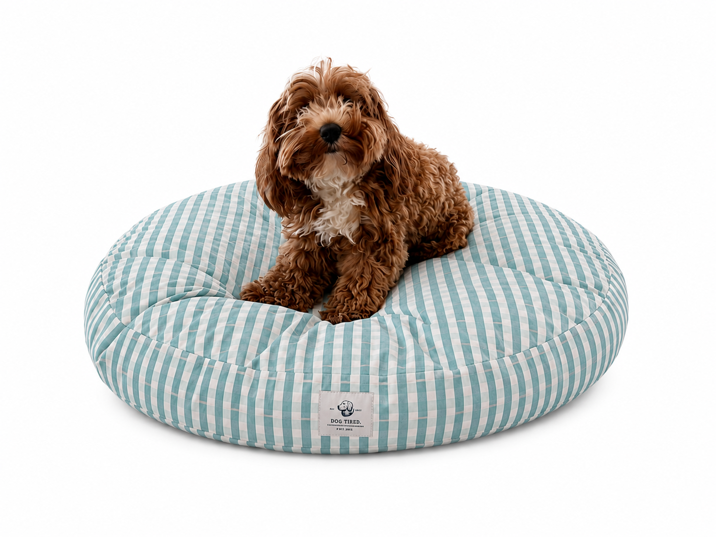 Dog lying on a blue and white striped donut designer pet bed with a visible brand label.
