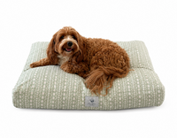 Dog lying on a designer dog bed with a sage green and white modern southwestern/ethnic cover design on a white background
