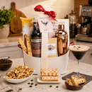 liquor Espresso martini cocktail Gift basket with drink mix, a copper cocktail shaker, popcorn, snacks on a kitchen counter.