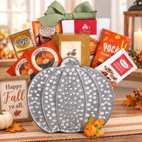 An autumn-themed gift basket, perfect for Thanksgiving, filled with seasonal treats in an adorable metal pumpkin container with boxed cookies, pumpkin spice mix, chocolate mix, and a green ribbon bow, styled on a table with fall decor.