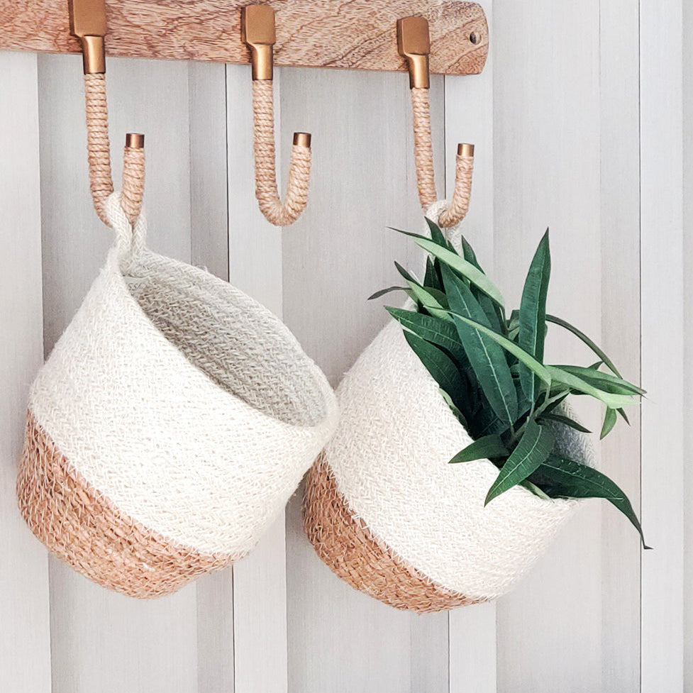Two hanging baskets in white and beige with a hanging handle on a white vertical panel background