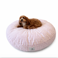 A small brown dog lies on a plush pink cat and dog donut bed on a white background.