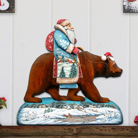 Decorative wall art of Santa Claus figure riding a bear on a wooden shelf.