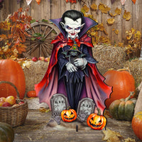 A Halloween yard sign featuring a Dracula vampire holding a small cat, surrounded by tombstones, jack-o'-lanterns, hay bales, pumpkins, and autumn leaves against a rustic wooden fence backdrop.