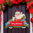 Decorative door hanger with Santa Claus driving a convertible car holding a 'Merry Christmas' sign, surrounded by festive decorations.