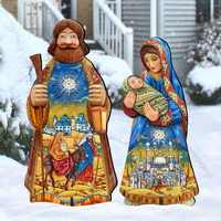 A decorative outdoor folk art Christmas nativity scene set featuring a standing wise man holding a scroll and a standing Mary holding baby Jesus, both with colorful printed robes and set in a snowy yard in front of a house.