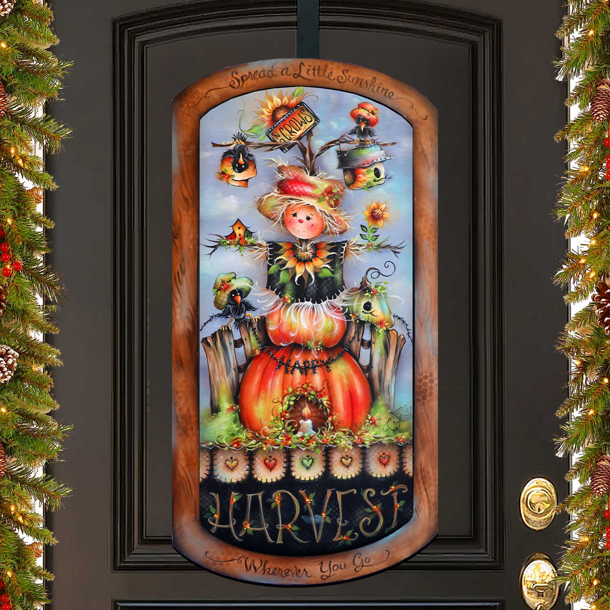 Decorative door hanging with scarecrow, pumpkins, and festive text on a black door.
