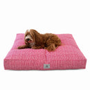 A small brown dog on a rectangle red dog bed with a subtle white grid pattern on a solid white background.