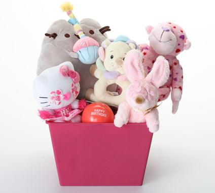 A pink dog toy gift basket filled with plush toys, including a white Hello Kitty figure, a pink bunny, a pink teddy bear, a gray plush, and a cream bear, with a small red 'Happy Birthday' ball, on a white background.