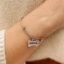 Silver bracelet with a 'Woof' charm on a wrist, wearing a beige sweater.