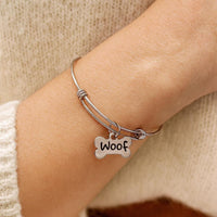 Silver bracelet with a 'Woof' charm on a wrist, wearing a beige sweater.