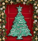 A modern green Christmas tree-shaped wooden sign with white holiday words and phrases, displayed on a red front door surrounded by festive garlands and ornaments.