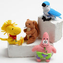 Four small plush cat toys arranged on white foam blocks against a light gray studio background: a yellow bird-like figure with a red neck scarf, a brown squirrel holding a nut, a blue-and-white bird perched on a block, and a pink star-shaped character wearing green and purple shorts.