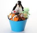 A collection of plush stuffed animals arranged inside a bright blue bucket on a clean white background. The toys include a penguin, a green turtle, an orange and white clownfish, a brown animal, and a small black-and-white chick.